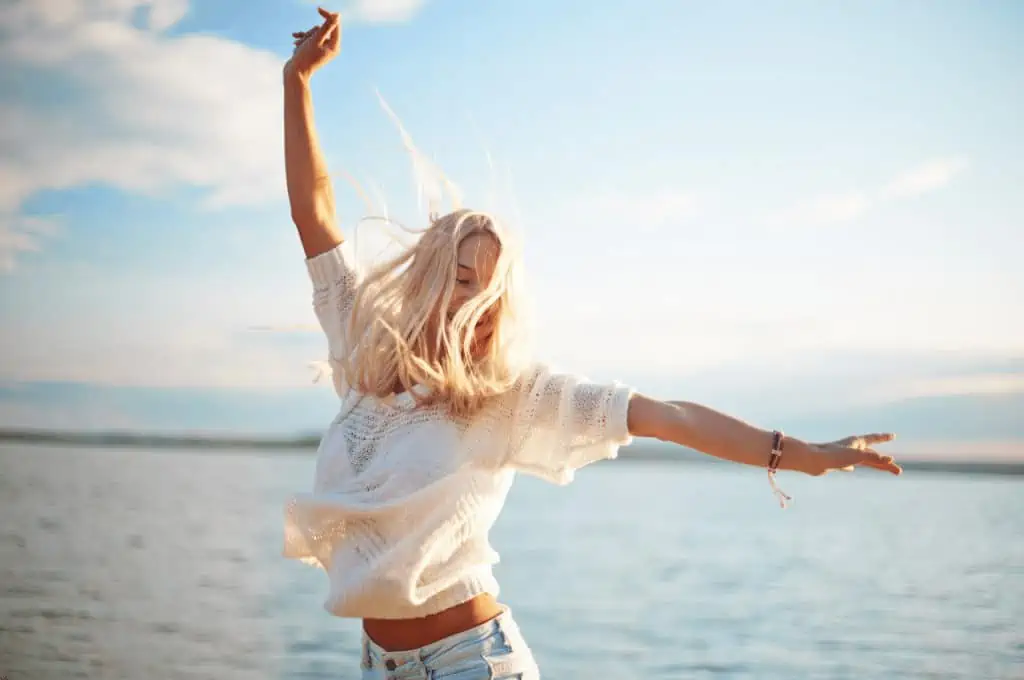 Woman happy and free on a beach with her hair blowing in the wind - Life Without Social Media: Is It Better?