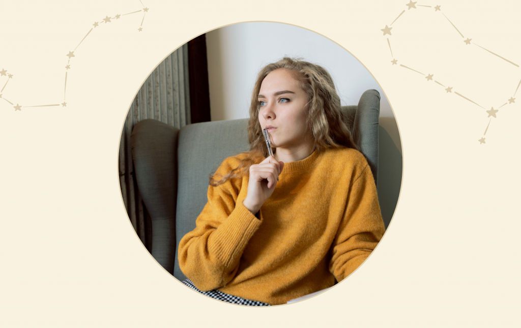 A woman in a yellow sweater sitting on a chair thinking with her hand on her chin