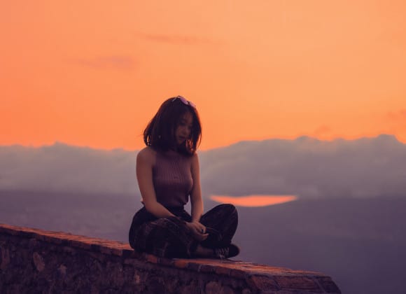 Girl sitting down cross legged with a sunset in the back ground