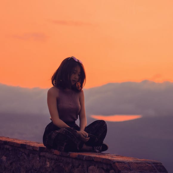 Girl sitting down cross legged with a sunset in the back ground