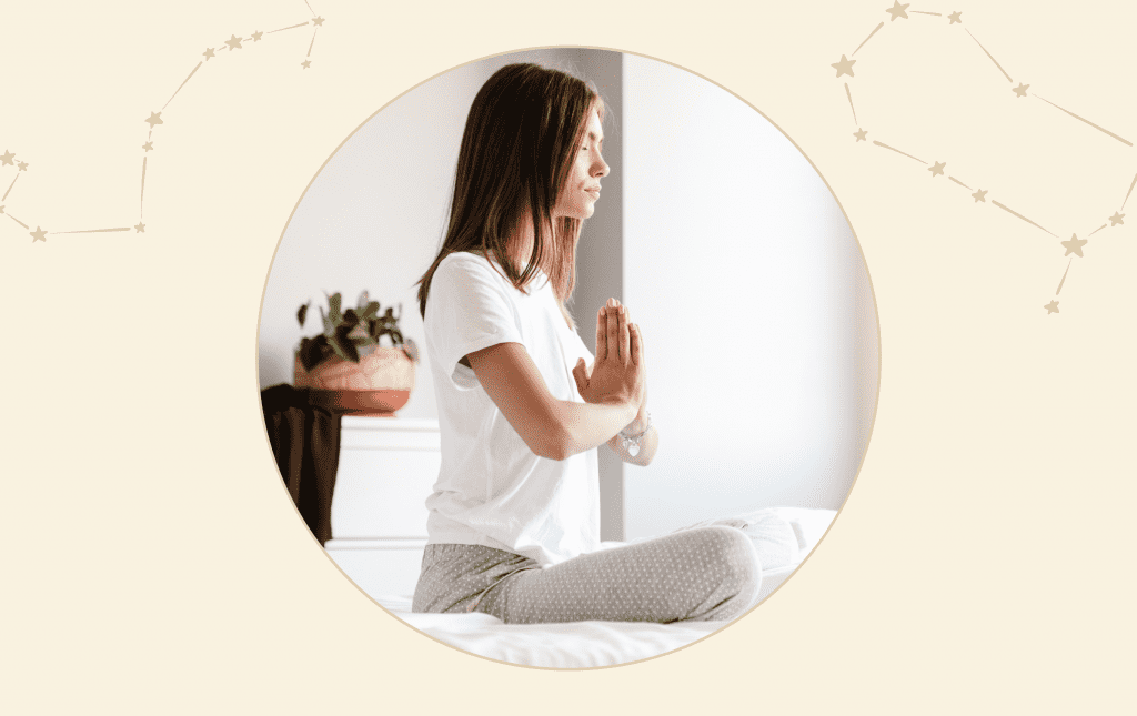 A woman sitting on a bed cross legged meditating with her hands together