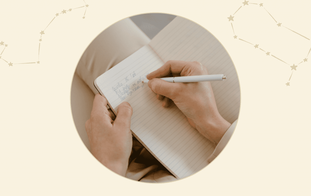 A person's hand holds a pen as they write in a notepad.