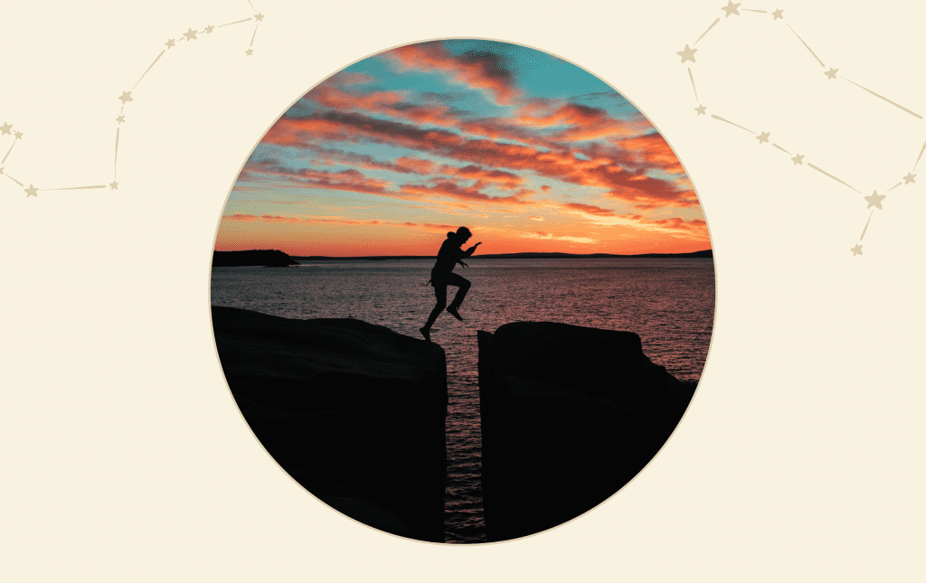 A man jumping between two rocks with a sunset and sea in the background.